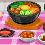 Na różowym obrusie znajduje się miska z różnorodnymi warzywami i grzybami, filiżanka zielonej herbaty, miseczki z kimchi, marynowanymi daniami i tofu