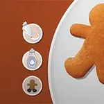 Ciasteczko w kształcie ludzika na okrągłym talerzu z trzema ikonami po lewej stronie, na tle w odcieniach brązu i bieli