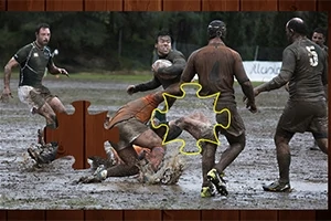 Grupa mężczyzn gra w rugby na błotnistym boisku, a na obrazie znajduje się brakujący element układanki