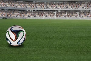 Piłka nożna leżąca na zielonej murawie stadionu z trybunami w tle