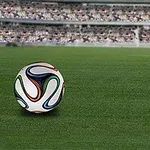 Piłka nożna leżąca na zielonej murawie stadionu z trybunami w tle
