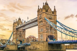 Tower Bridge w Londynie o zachodzie słońca, z widocznymi wieżami i fragmentem mostu, oraz zabudowania w tle