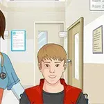 Młoda kobieta w stroju pielęgniarki z ręką na ramieniu chłopca na wózku inwalidzkim w korytarzu szpitalnym