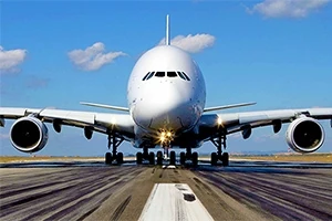 Duży samolot pasażerski widziany z przodu na pasie startowym, niebo z kilkoma chmurami w tle